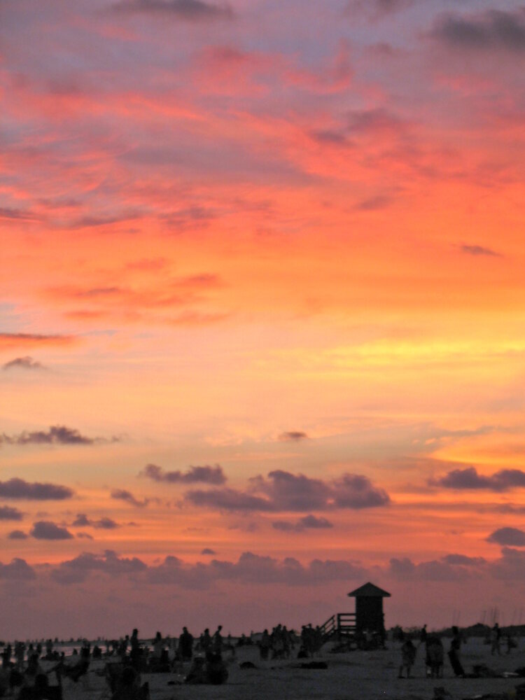 Beachgoers watching a vivid sunset over the Gulf of Mexico at Siesta Key